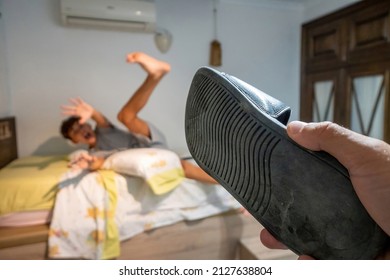 Hand Of A Person With A Slipper Threatening A Screaming Teenager In Bed