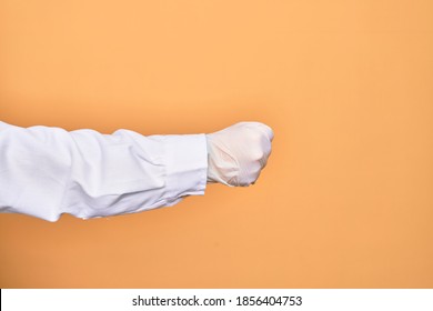 Hand Of A Person Wearing Medical Surgical Glove Doing Protest Gesture With Fist Over Isolated Yellow Background