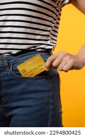 hand of person woman holding plastic credit card out of the pocket blue jean plants isolated on yellow studio background. online shopping payment, currency, bill, pay money, finance concept. - Shutterstock ID 2294800425