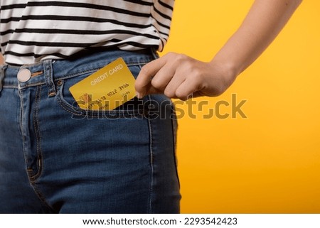 hand of person woman holding plastic credit card out of the pocket blue jean plants isolated on yellow studio background. online shopping payment, currency, bill, pay money, finance concept.