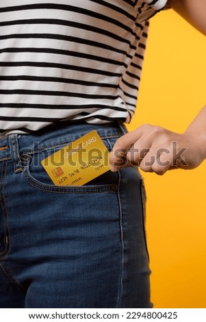 hand of person woman holding plastic credit card out of the pocket blue jean plants isolated on yellow studio background. online shopping payment, currency, bill, pay money, finance concept.