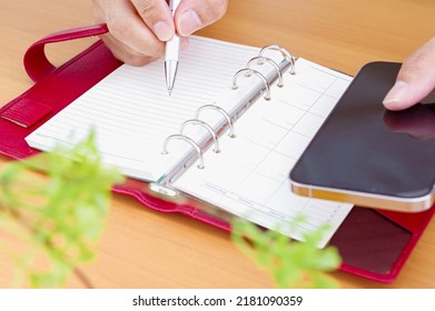 Hand Of A Person Writing A Notebook While Looking At Hisher Phone