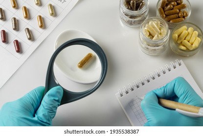 Hand of a pharmacist holds a capsule with dietary supplements and magnifying glass on the background of jars of ingredients in laboratory - Shutterstock ID 1935538387