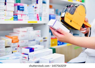 Hand Of The Pharmacist Using Yellow Labeling Gun For Sticking Price Label Of Medicine In Pharmacy Drugstore.