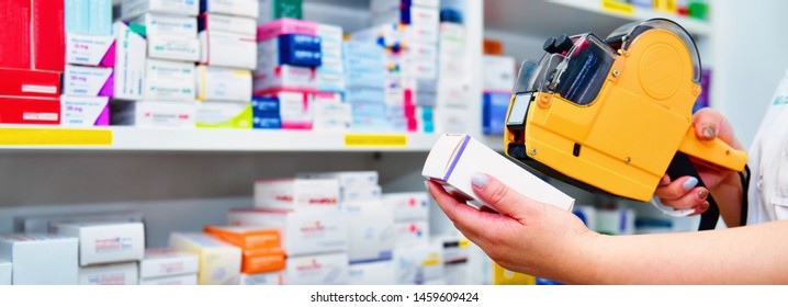 Hand Of The Pharmacist Using Yellow Labeling Gun For Sticking Price Label Of Medicine In Pharmacy Drugstore.banner Size