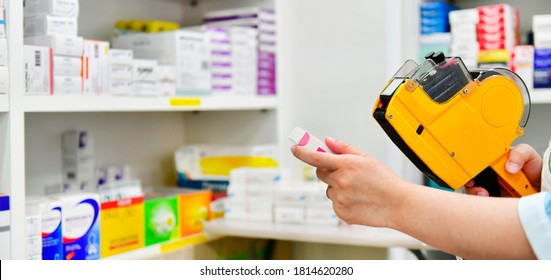 Hand Of The Pharmacist Using Yellow Labeling Gun For Sticking Price Label Of Medicine In Pharmacy Drugstore.copy Space