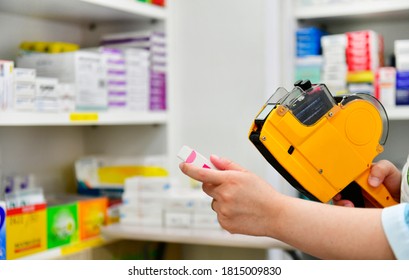 Hand Of The Pharmacist Using Yellow Labeling Gun For Sticking Price Label Of Medicine In Pharmacy Drugstore.