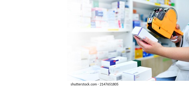 Hand Of The Pharmacist Using Yellow Labeling Gun For Sticking Price Label Of Medicine In Pharmacy Drugstore. Copy Space