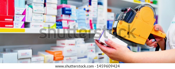 Hand\
of the pharmacist using yellow labeling gun for sticking price\
label of medicine in pharmacy drugstore.banner\
size