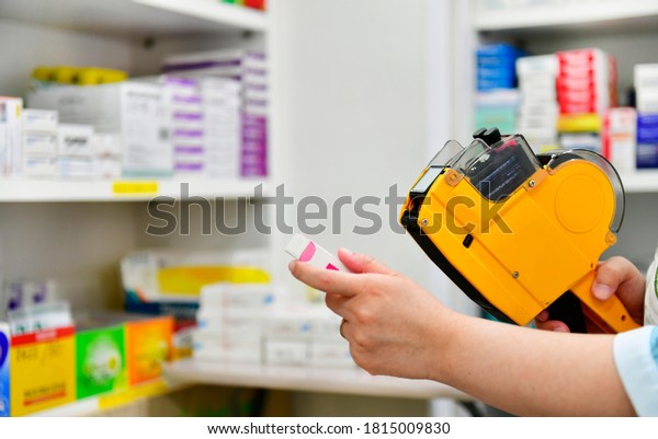 Hand of the\
pharmacist using yellow labeling gun for sticking price label of\
medicine in pharmacy\
drugstore.
