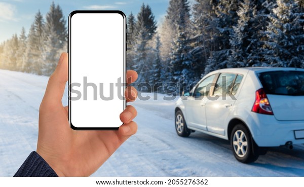 Hand with a phone on the\
background of a car behind a winter road. Blank screen, you can add\
your content