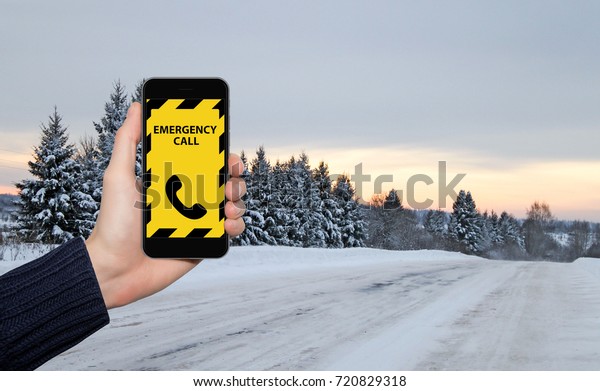Hand with phone on a background of a winter\
road. Emergency call\
concept.