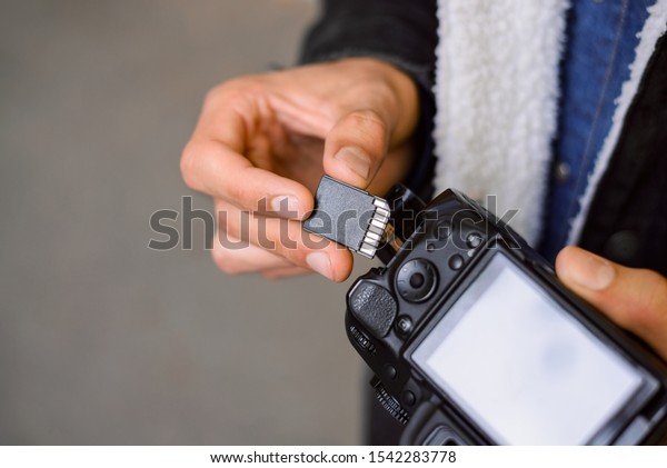 Hand of photographer holding SD memory Card. Male\
photographer changing SD card of a photo camera outdoors. Young\
photographer has run out of storage on his memory stick, changes\
card on his dslr