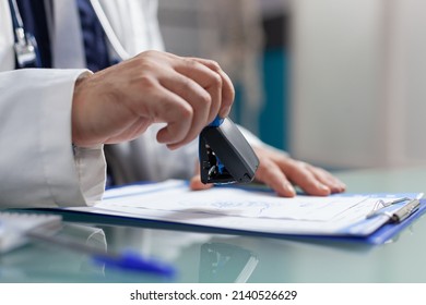 Hand Of Physician Using Medical Seal On Prescription Paper In Cabinet. Health Care Specialist Putting Stamp On Checkup File To Give Treatment To Patient At Consultation Appointment. Close Up