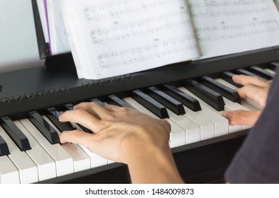 Hand of Piano Player on White Keys and Black Keys of Electric Piano with Piano Staff or Sheet Music
