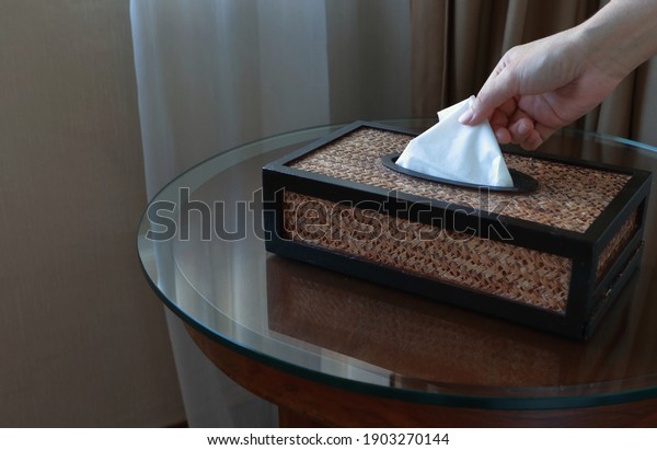 Hand picking clean facial tissue from brown\
tissue box on glass table in hotel\
room.