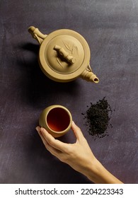 Hand Picking Up A Cup Of Black Tea, Next To A Ceramic Teapot