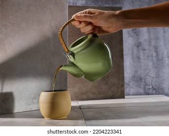 Hand Picking Up A Green Teapot, Pouring Tea Into A Cup