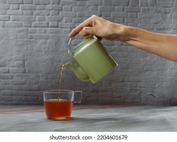 Hand Picking Up A Green Teapot, Pouring Tea Into A Glass Cup