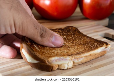 Hand Picking Up A Hot Cheese Sandwich With Toasted Bread On A Wooden Surface