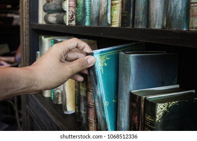 Hand picking an old book from rustic shelf, searching for knowledge
