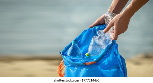 Hand Picking Up Plastic Bottles Into Blue Trash Bag. Cleaning On The Beach. Copy Space