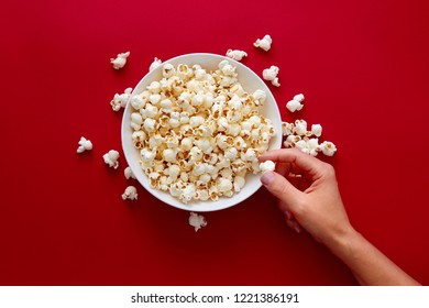 Hand Picking Popcorn In White Bowl Against Red Background. 