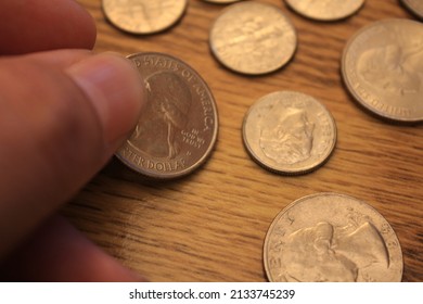 Hand Picking Up A Quarter Coin In American Currency Spread On The Wooden Floor