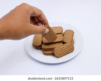 Mano que recoge una galleta rectangular de un plato lleno de galletas, fijado en un fondo blanco