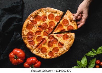 Hand Picking Slice Of Pepperoni Pizza. Pizza Party. Hot Italian Pepperoni Pizza On Black Concrete Background, Top View