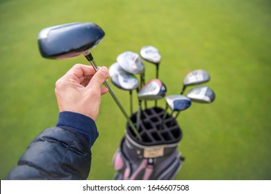 hand picks a golf club out of a bag on a green golf course