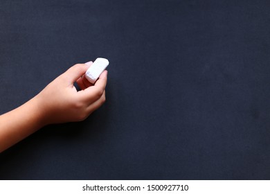 Сhild hand with a piece of white chalk on the school blackboard background