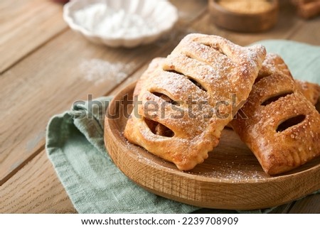 Hand pies. Mini puff pastry or hand pies stuffed with apple and sprinkle sugar powder in wooden plate. Homemade pie snack with crust for breakfast rustic photo.  Copy space.