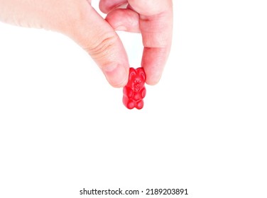 Hand Pinch Holding And Squeezing A Red Gummy Bear Candy Isolated On White Background, Close-up.