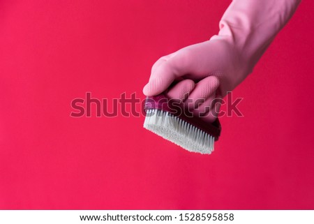 Hand in pink latex protective glove with dust brush on pink background. Cleaning and housework work concept