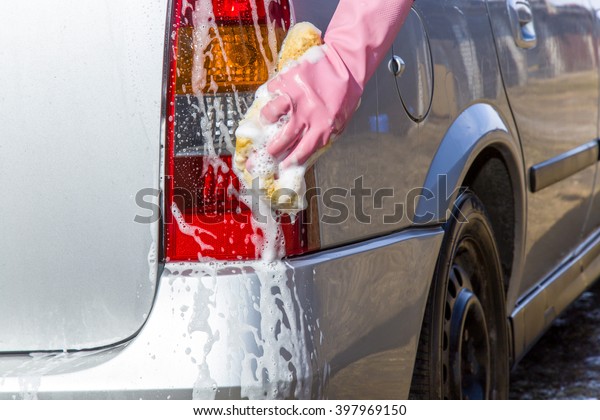 Hand in pink protective glove washing a cars back\
lamp with sponge. Early spring washing or regular wash up.\
Professional car wash by\
hands.