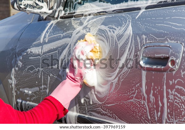 Hand in pink protective glove washing a silver car\
with sponge. Early spring washing or regular wash up. Professional\
car wash by hands.