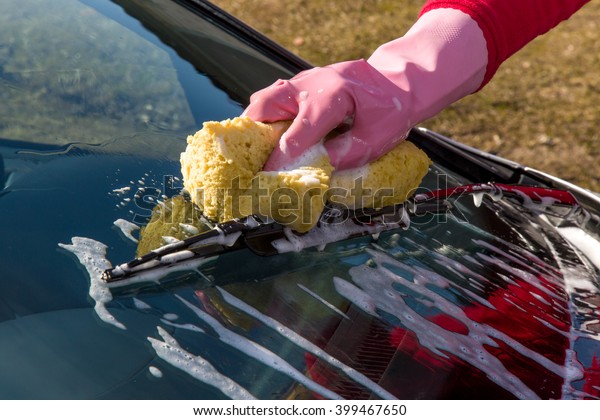 Hand in pink\
protective glove washing a silver cars window and windshield wipers\
with sponge. Early spring washing or regular wash up. Professional\
car wash by hands.