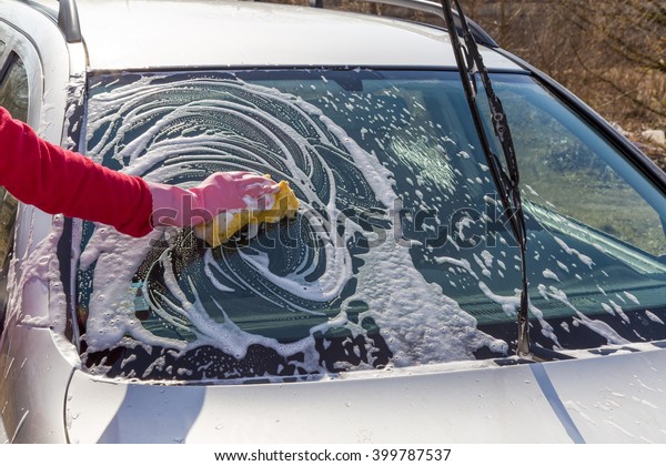 Hand in pink\
protective glove washing a cars window with sponge. Early spring\
washing or regular wash up.\
