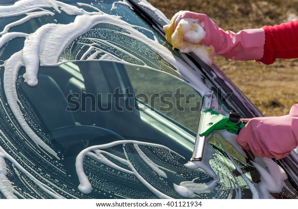 Hand in pink protective glove washing a\
cars window with professionally squeegee. Early spring washing or\
regular wash up. Professional car wash by\
hands.