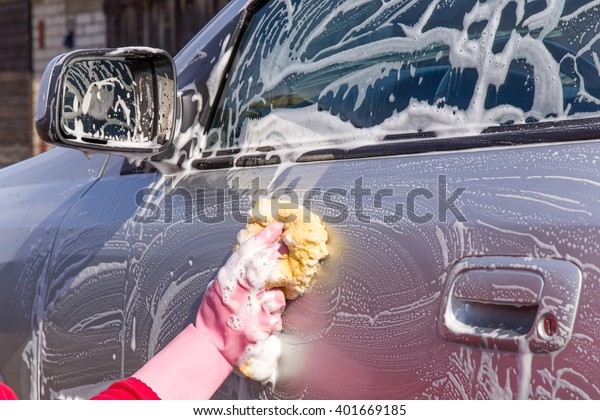 Hand in pink protective glove washing a silver car\
with sponge. Early spring washing or regular wash up. Professional\
car wash by hands.