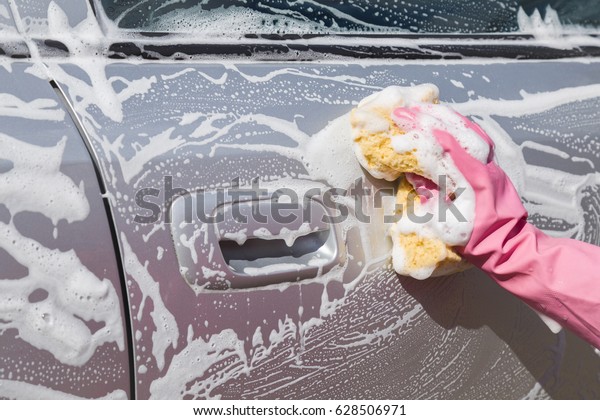 Hand in pink protective glove washing\
a silver car\'s door with sponge in sunny day. Early spring washing\
or regular wash up. Professional car wash by\
hands.