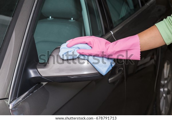 Hand in pink protective\
glove wiping a car mirror with microfiber cloth in the garage.\
Early spring washing or regular wash up. Professional car wash by\
hands.