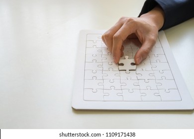 Hand places a piece of the white jigsaw puzzle to full field the gap of the jigsaw to make the puzzle completely finish, represent businessman or someone finishes the job. - Powered by Shutterstock