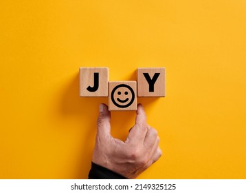 Hand places the word joy on wooden blocks with a smiling face symbol. Joy, happiness, pleasure, joyful emotion.