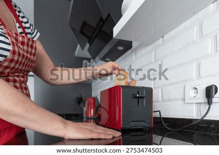 Hand placing bread slices into red kitchen toaster on black countertop in modern home kitchen interior