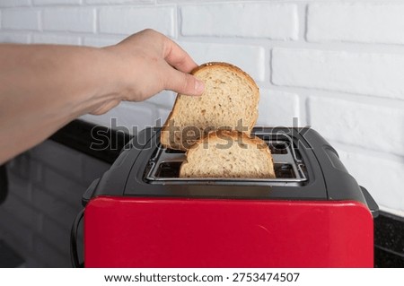 Hand placing bread slices into red kitchen toaster on black countertop in modern home kitchen interior