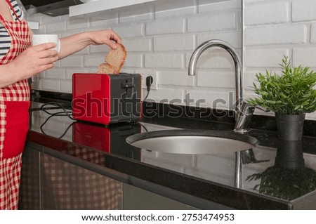 Hand placing bread slices into red kitchen toaster on black countertop in modern home kitchen interior