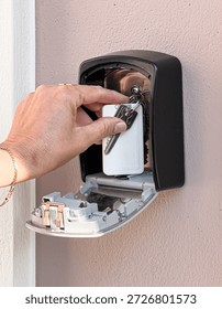 Hand placing keys inside a combination lock key safe box mounted on an outdoor wall
