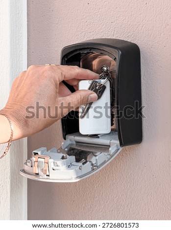 Hand placing keys inside a combination lock key safe box mounted on an outdoor wall